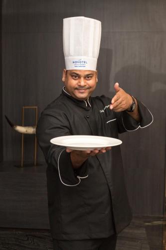 a man wearing a chef hat holding a plate at Novotel Chennai Chamiers Road in Chennai