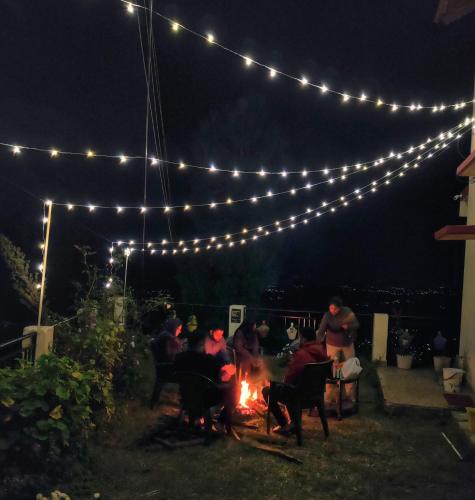 a group of people sitting around a fire at night at Meraki - Entire 3BHK Villa With Himalayan Views in Rānīkhet