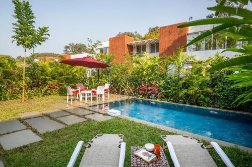 a pool with chairs and a table and an umbrella at La Zamora, 3BHK Villas near Vagator & Anjuna Beach, North Goa with Private Pool, Garden, Terrace & Security in Assagao