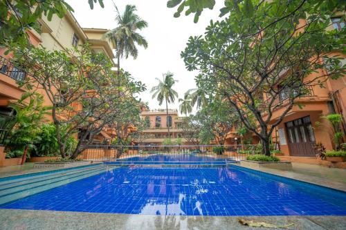 a swimming pool in a courtyard with trees and a building at Neelams The Grand Hotel in Calangute