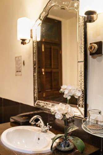 a bathroom sink with a mirror and a vase with flowers at Hotel Penaga in George Town
