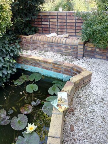 un jardin avec un étang avec un banc et des nénuphars dans l'établissement Les Roses de Rita, à Boisset-lès-Montrond