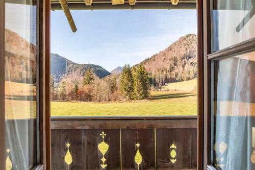 a window with a view of a field and mountains at Ferienwohnung Karwendelblick in Jachenau