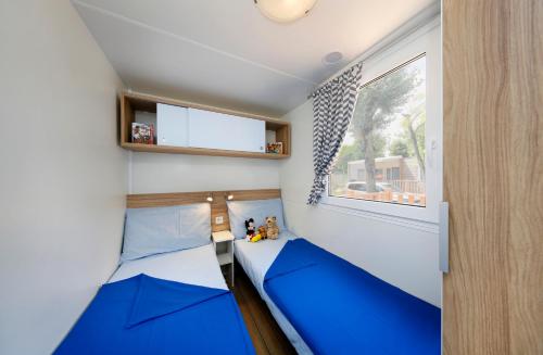um pequeno quarto com duas camas azuis e uma janela em Albatross Mobile Homes on Camping Laguna Village em Porto Falconera