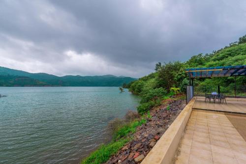 a dock with a table and chairs next to a body of water at SaffronStays Riverdale, Mulshi - Lakefront villa with pool and mountain view in Pune