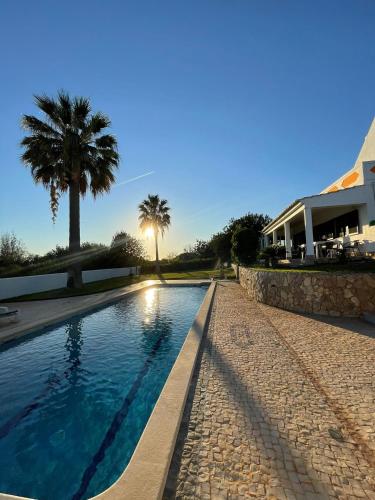 a swimming pool with a palm tree and a house at Casa Esperança - carefree living with big private pool and great views in Olhão