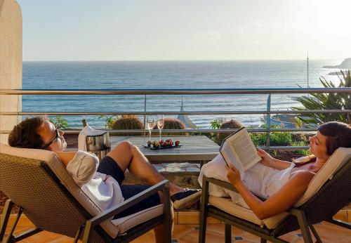 two people sitting in chairs on a balcony looking at the ocean at H10 Playa Meloneras Palace in Meloneras