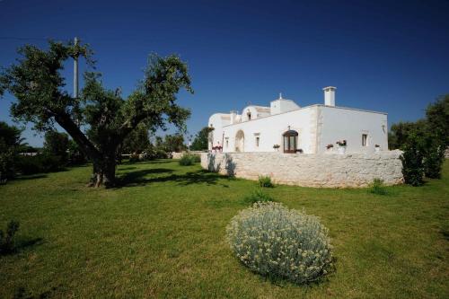 a white house with a tree in a field at Agriturismo Arco di Sole in Alberobello