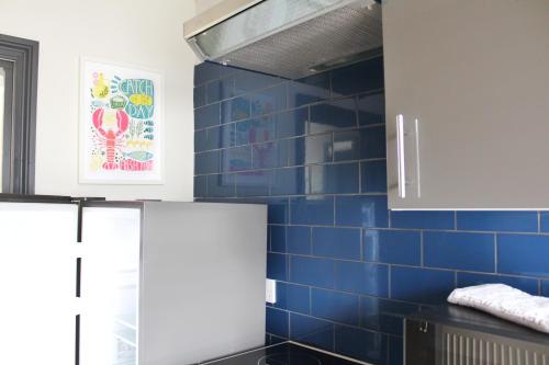 a kitchen with blue tiled walls and white cabinets at Small Home Big Welcome in Margate