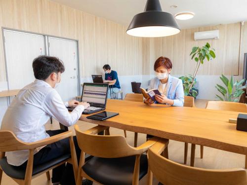 two people sitting at a table with a laptop at ゲストハウス五島時光 in Goto