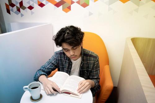 a young man sitting at a table reading a book at Tuju Arteri Pods in Jakarta