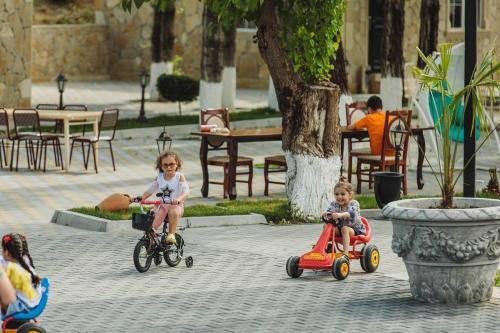 two children riding bikes and scooters in a courtyard at Mehsul Recreational Center in İsmayıllı