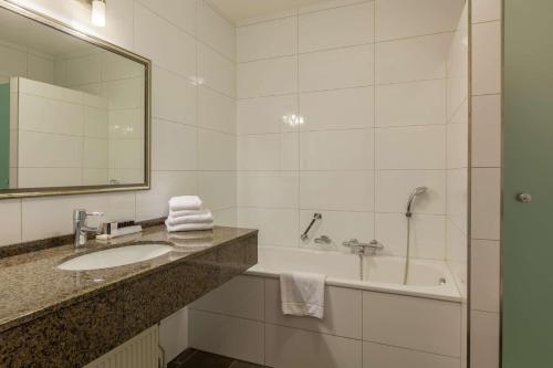 a bathroom with a sink and a tub and a mirror at Best Western Hotel Nobis Eindhoven-Venlo A67 in Asten