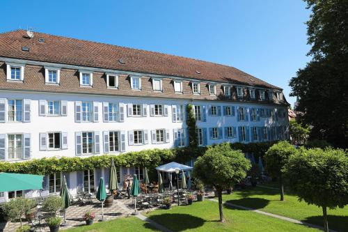 a large white building with chairs and umbrellas in a park at Bad Hotel Überlingen in Überlingen