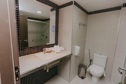 a bathroom with a toilet and a sink and a mirror at Pajuçara Praia Hotel in Maceió