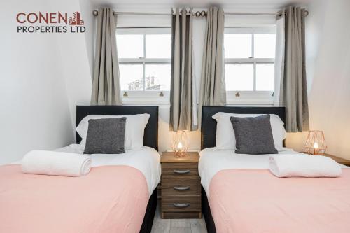 two beds in a bedroom with two windows at CONEN Aplite Apartment in London