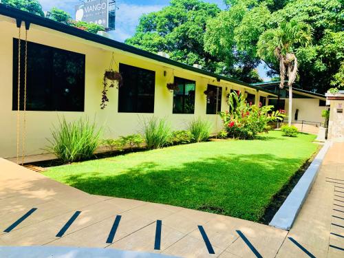 a yellow house with a yard of grass and flowers at Hotel Mango Airport in Alajuela City