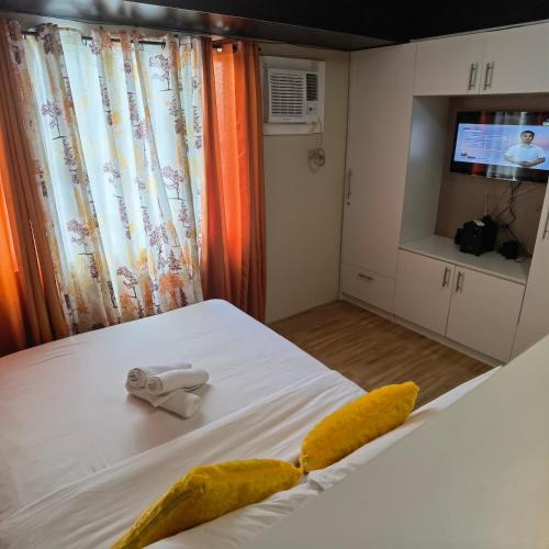 a bedroom with a white bed with yellow pillows and a tv at Avida Davao by davaobnb & Lemonique Homes in Davao City