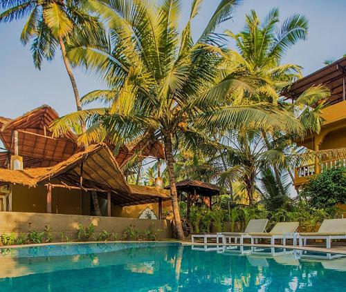 a swimming pool in front of a resort with palm trees at juSTa Morjim Beach Resort Goa - 80 Steps from Morjim Beach in Morjim