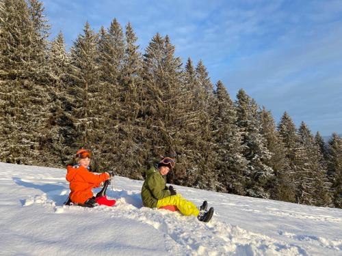two people sitting in the snow on a snow covered slope at MONDI Resort und Chalet Oberstaufen in Oberstaufen