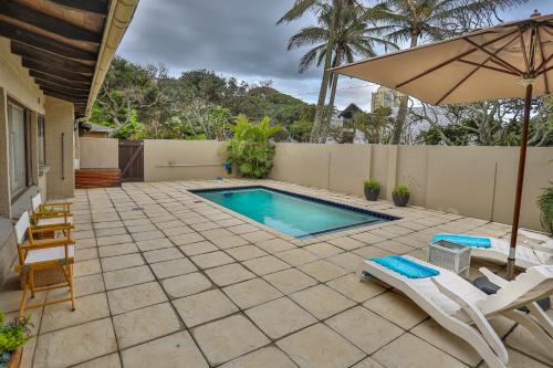 a swimming pool with two chairs and an umbrella at One Jack Powell House- Classic family home steps away from the beach in Ballito