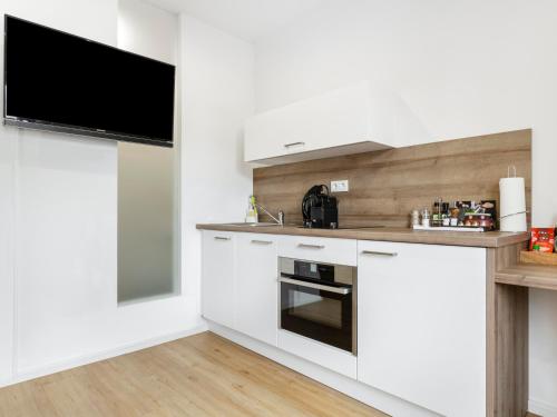 a kitchen with white cabinets and a flat screen tv at limehome Augsburg Am Katzenstadel in Augsburg