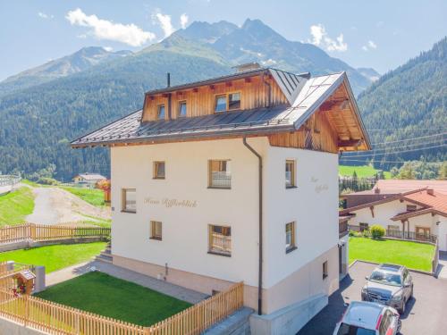 a house with a wooden roof with mountains in the background at Appartement Rifflerblick in Pettneu am Arlberg