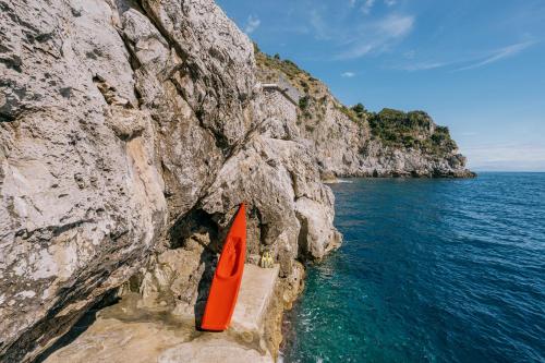 a red kayak sitting on a cliff next to the water at Villa Eris Amalfi Coast in Conca dei Marini