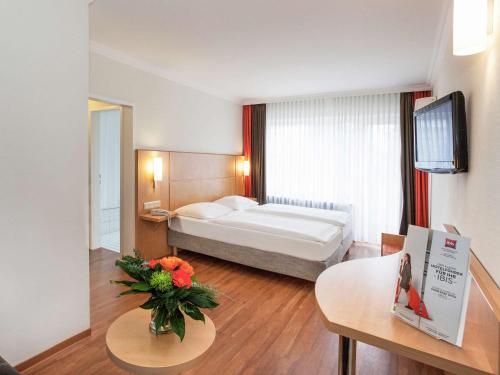 una habitación de hotel con una cama y una mesa con flores en ibis Saarbrücken City, en Saarbrücken