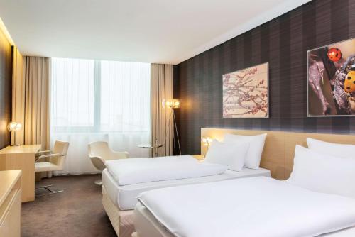 a hotel room with two beds and a desk at NH Bratislava Gate One in Bratislava