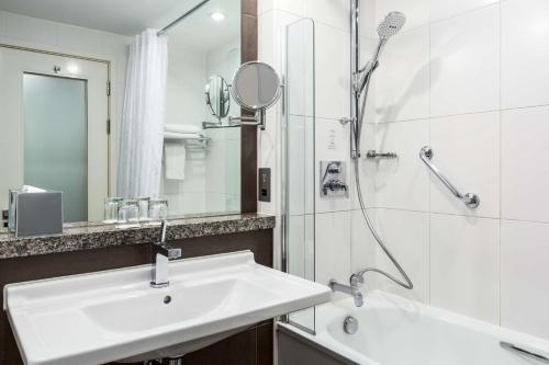 a bathroom with a sink, mirror, and bathtub at NH London Kensington in London