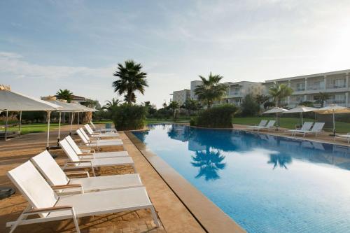 a pool with white lounge chairs and umbrellas at Radisson Blu Resort Saidia Beach in Saidia 
