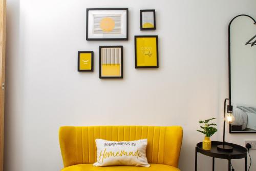 a yellow couch in a living room with pictures on the wall at Charles Alexander Short Stay - Charnley House Apartments in Blackpool