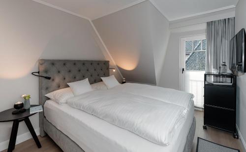 a white bedroom with a large white bed and a window at Jaumann's Südwind Sylt in Westerland (Sylt)