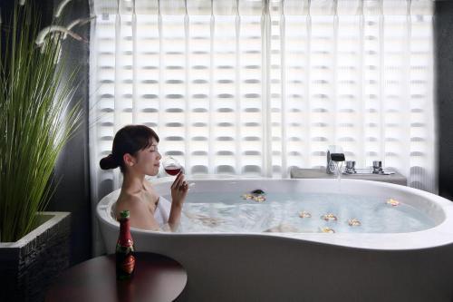 una mujer sentada en una bañera bebiendo una copa de vino en Hotel Gate In Kagoshima Tenmonkan, en Kagoshima
