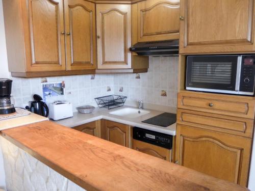 La cuisine est équipée de placards en bois, d'un évier et d'un four micro-ondes. dans l'établissement Apartment Le Capricorne by Interhome, à Cabourg