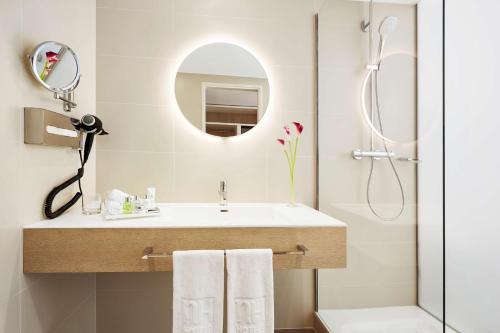 ein Bad mit einem Waschbecken, einem Spiegel und einer Dusche in der Unterkunft NH Collection Hamburg City in Hamburg