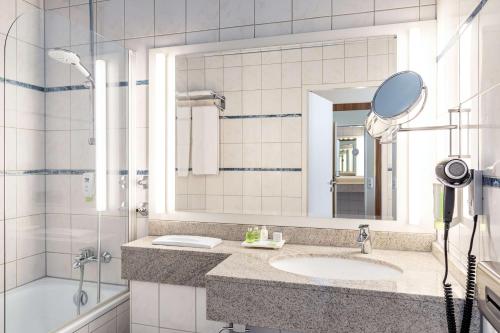 uma casa de banho com um lavatório, um espelho e um chuveiro em NH Ingolstadt em Ingolstadt