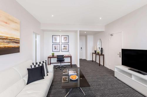a living room with a white couch and a television at Radisson On Flagstaff Gardens Melbourne in Melbourne
