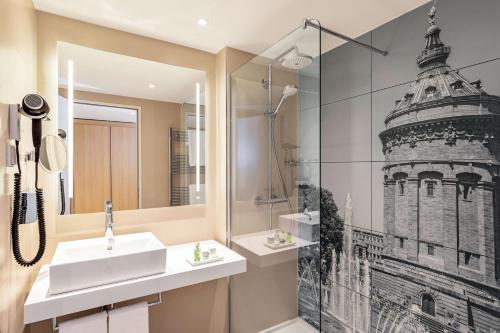 a bathroom with a sink and a shower with a picture of a tower at NH Mannheim in Mannheim