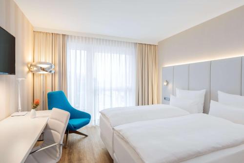 Cette chambre d'hôtel comprend deux lits et une chaise bleue. dans l'établissement NH Mannheim, à Mannheim