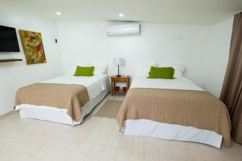 two beds in a white room with green pillows at Angeli Gardens Boutique Hotel in San Pedro Sula