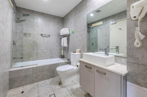 a bathroom with a toilet and a tub and a sink at Argus Hotel Darwin in Darwin