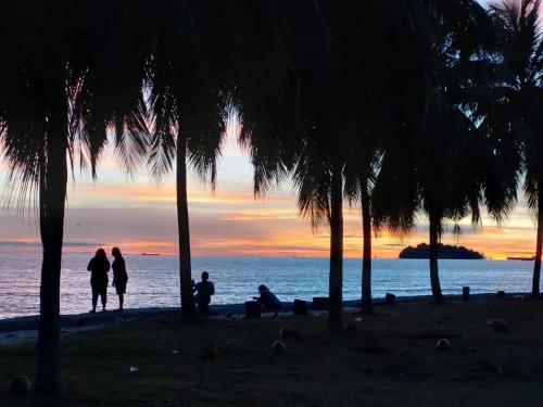 a group of people sitting on the beach at sunset at Port Dickson PD Beach Front Homestay in Port Dickson