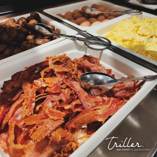 a plate of food with bacon and eggs and other foods at Hotel Am Triller - Hotel & Serviced Apartments in Saarbrücken