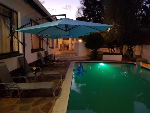 a swimming pool with a blue umbrella and chairs at The Royal Princess B&B on Malibongwe Drive in Johannesburg