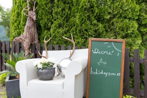 a chalkboard sign next to a white chair with flowers at Forest Chalet, 15 min to salzburg olt town, and most beautiful lakes, secluded location, 1,000 sqm garden, mountainview, panorama sauna, bath whirlpool, BBQ&bikes&sunbeds for free, up to 10 p in Golling an der Salzach