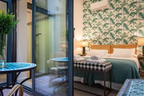 Habitación con cama, mesa y puerta de cristal. en La Casa del Pintor Apartments, en Sevilla
