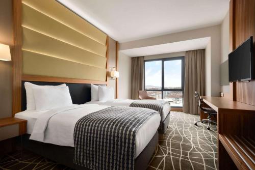 um quarto de hotel com duas camas e uma secretária em Ramada By Wyndham Elazığ em Elazig