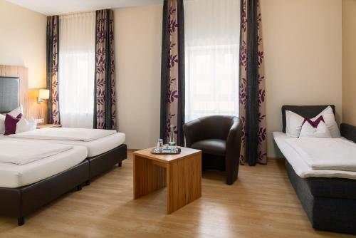 a room with two beds and a chair and a table at ClassicX Landhaus & Hotel - Bed & Breakfast in Gensingen